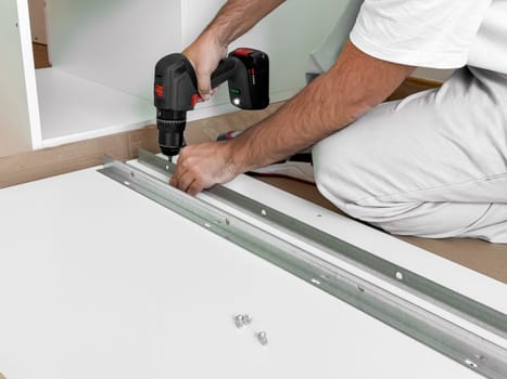 Caucasian male adult assembling furniture with electric drill in workshop.