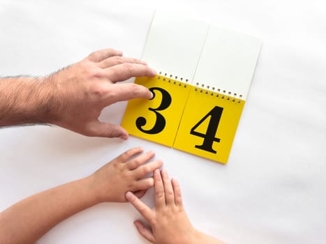 Father and child turn over page of calendar with large numbers.