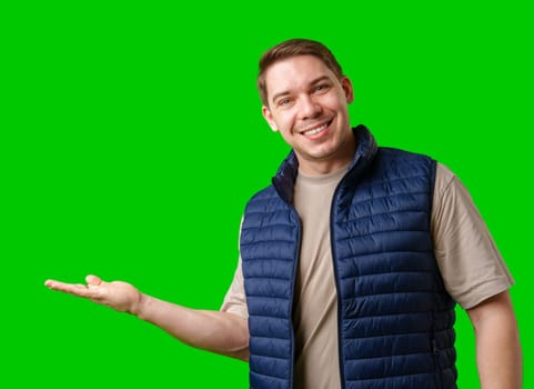 Man in a navy vest gestures while standing against a bright green background in studio