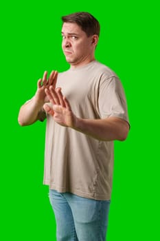 A man with a neutral expression gestures defensively against a bright green background in studio