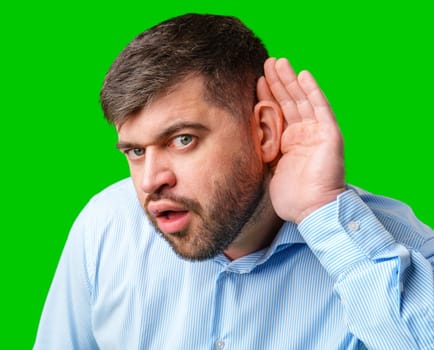 A man listening intently with a surprised expression in a bright green background in studio