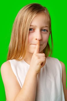 Young girl playfully signaling for silence with a finger to her lips against a vibrant green background in studio