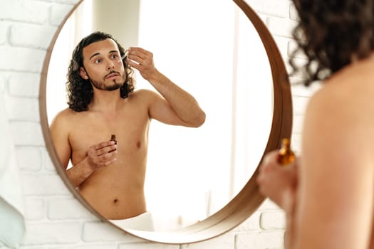 A close-up of a man applying a serum drop to his face, showcasing skincare routine