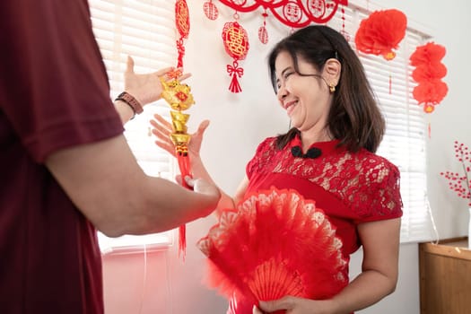 An elderly couple joyfully celebrates Chinese New Year at home surrounded by vibrant decorations and festive spirit.