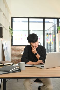 Young businessman speaking on mobile phone while working on his laptop at modern office.