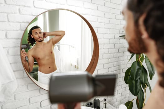 A man with curly hair styles himself in a bright room while using a hairdryer to enhance his look close up