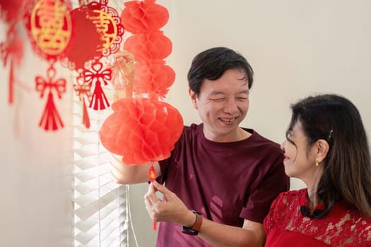 An elderly couple joyfully decorates their home with lanterns for Chinese New Year celebrating love and tradition together.