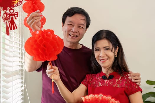 An elderly couple joyfully decorates their home with lanterns for Chinese New Year embodying tradition and love.