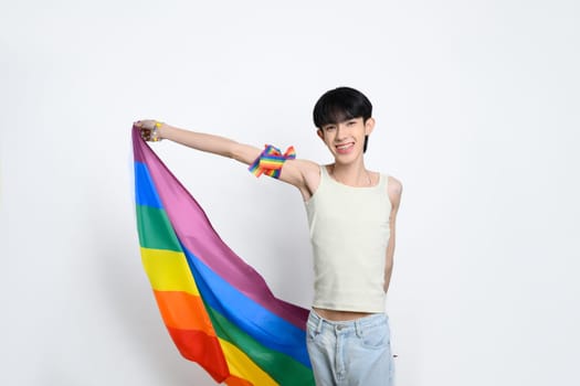 Smiling man proudly displaying a rainbow flag on white background. LGBTQ pride and equality concept.