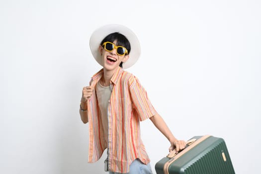 Joyful man wearing summer outfit and sunglasses posing with a suitcase ready for upcoming trip.