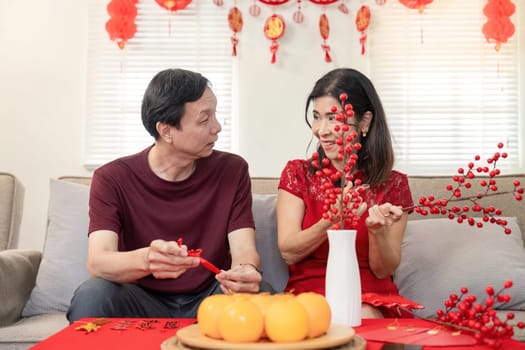 An elderly couple joyfully decorates their home for Chinese New Year symbolizing love and tradition in a festive atmosphere.