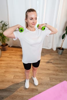 A woman exercises with green dumbbells at home in a bright room filled with light and plants