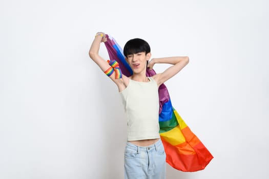 Cheerful young gay man holding a rainbow pride flag on white background. LGBTQ pride and equality concept.