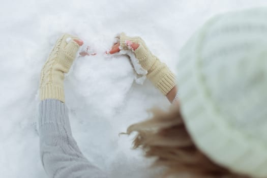 Close-up Snow heart in hands in knitted gloves on the background of snow cover. Valentine's Day.