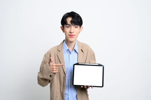 Young man pointing finger at empty digital tablet over white background, for business or tech presentations.