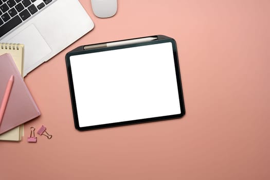 Top view digital tablet with empty screen, laptop and stationery on a pink pastel background.