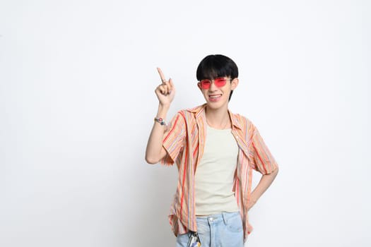 Confident young man wearing sunglasses pointing fingers at copy space over white background.