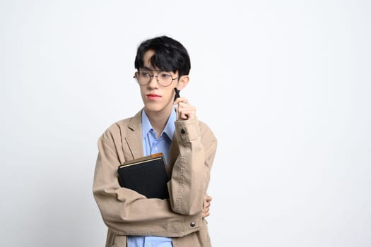 Thoughtful young businessman in glasses holding notebook and pen, appearing deep in thought.