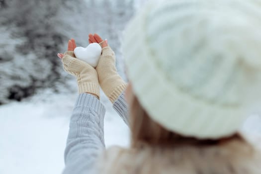 I like winter. Portrait of a happy young girl holding a snowy heart in her hand during winter time. Valentine's Day