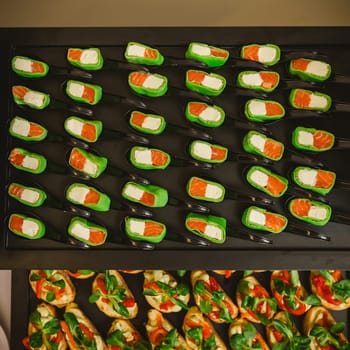 Platter of gourmet appetizers featuring pieces of salmon and cream cheese wrapped in a green wrap, served on black spoons. The presentation is elegant and suitable for catering events or parties