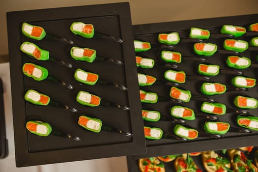 Platter of gourmet appetizers featuring pieces of salmon and cream cheese wrapped in a green wrap, served on black spoons. The presentation is elegant and suitable for catering events or parties