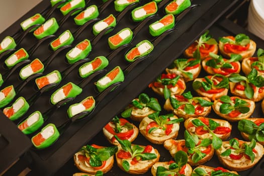 Platter of gourmet appetizers featuring pieces of salmon and cream cheese wrapped in a green wrap, served on black spoons. The presentation is elegant and suitable for catering events or parties