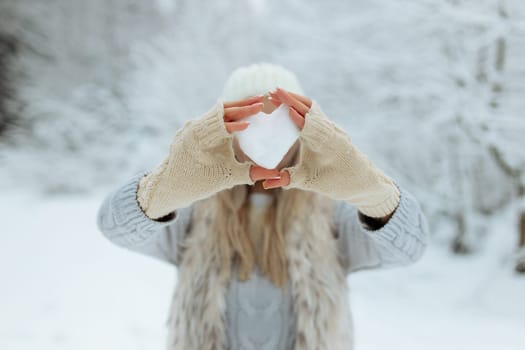Close-up girl holds a snowy heart in front of her in gloves.