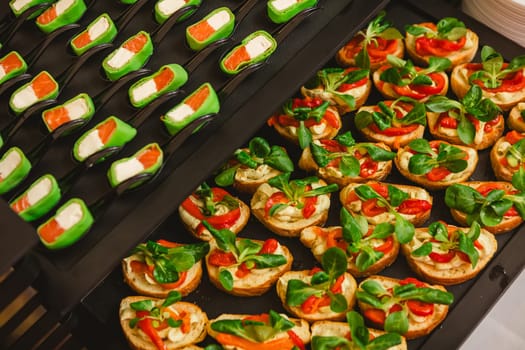 Platter of gourmet appetizers featuring pieces of salmon and cream cheese wrapped in a green wrap, served on black spoons. The presentation is elegant and suitable for catering events or parties