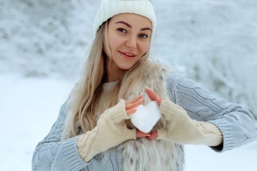 I like winter. Portrait of a happy young girl holding a snowy heart in her hand during winter time. Valentine's Day