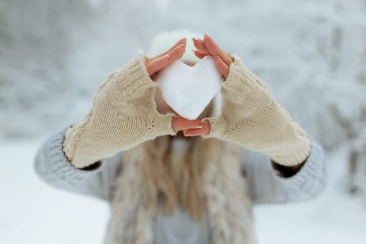 Close-up girl holds a snowy heart in front of her in gloves.
