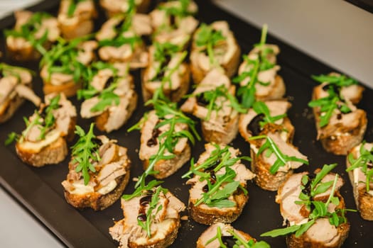 A tray of gourmet bruschetta appetizers featuring slices of bread topped with meat, arugula, and a drizzle of balsamic glaze, perfect for parties or gatherings.