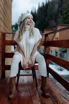 A sexy girl in a white sweater and stockings on the balcony admires the beauty of nature. wool clothes and a hat on a beautiful blonde.