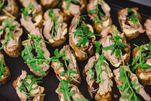 A tray of gourmet bruschetta appetizers featuring slices of bread topped with meat, arugula, and a drizzle of balsamic glaze, perfect for parties or gatherings.