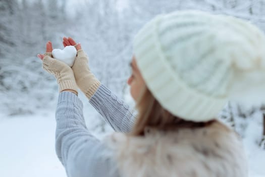 I like winter. Portrait of a happy young girl holding a snowy heart in her hand during winter time. Valentine's Day