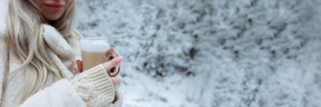 A beautiful blonde in winter clothes holds a cappuccino mug in her hands. A place for text gentle snow background.