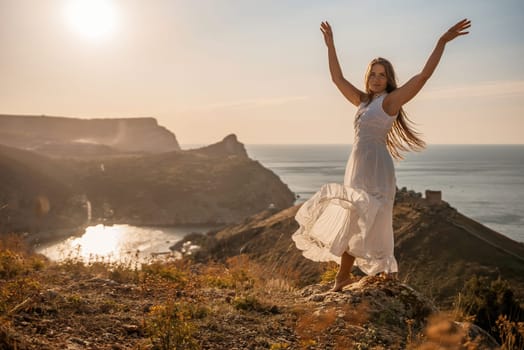 A woman stands on a hill overlooking the ocean. She is wearing a white dress and has long hair. The scene is serene and peaceful, with the sun shining brightly in the background