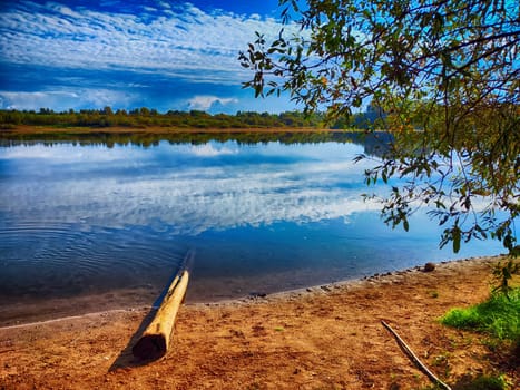 The picturesque river flows gently, surrounded by lush greenery and bathed in sunlight, evoking a peaceful spring atmosphere.
