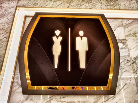 A stylish restroom sign features clear male and female icons, set against a well-lit marble wall, indicating facilities.
