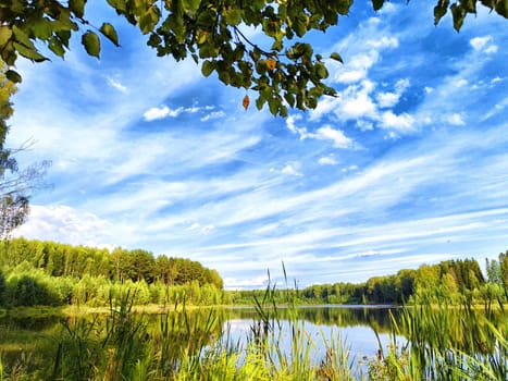The river reflects the vivid blue sky filled with wispy clouds, framed by verdant trees on both sides, creating a tranquil vista.