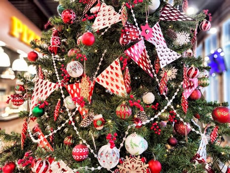 A beautifully adorned Christmas tree stands in a lively indoor area, featuring red and white decorations, ornaments, and garlands.