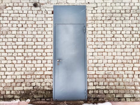 Gray door integrated into a textured brick wall, highlighting natural light and outdoor setting on a clear day.