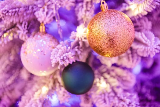 A close-up of a Christmas tree adorned with glittery ornaments. The image features a gold glitter ball, a white ornament with gold specks, and a dark green bauble, all hanging on frosted branches.