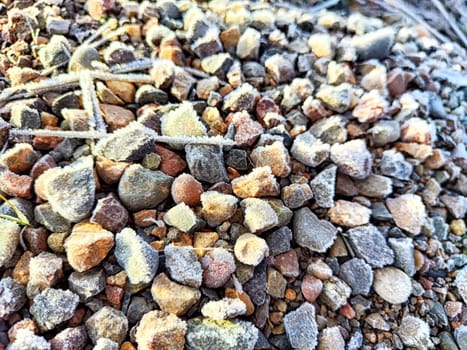 Frost covers gravel stones, creating a unique texture and pattern amidst delicate crystals in the fresh morning air.