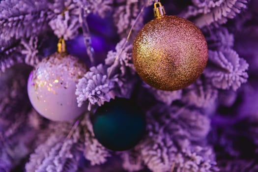 A close-up of a Christmas tree adorned with glittery ornaments. The image features a gold glitter ball, a white ornament with gold specks, and a dark green bauble, all hanging on frosted branches.