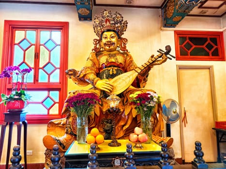 Hong Kong - April 08, 2024: At Po Lin Monastery, a vibrant statue with an instrument is nestled among flowers and offerings, radiating tranquility.
