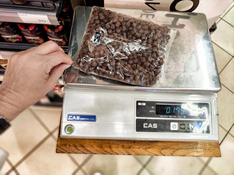 Kazan, Russia - August 27, 2024: A person holds a bag of bulk food while measuring the weight on a digital scale in a grocery store setting.