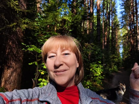 Woman takes a cheerful selfie in a lush forest while exploring nature with her dog on a bright, sunny day.