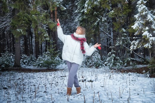 A middle-aged woman dressed warmly walks through a snow-covered forest, celebrating the joy of winter with decorations.