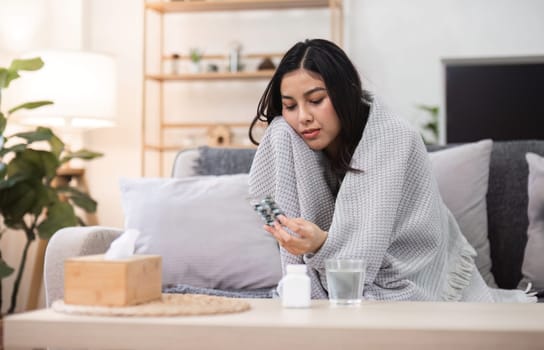 A young woman sits at home feeling unwell pondering her health while surrounded by a comforting environment.