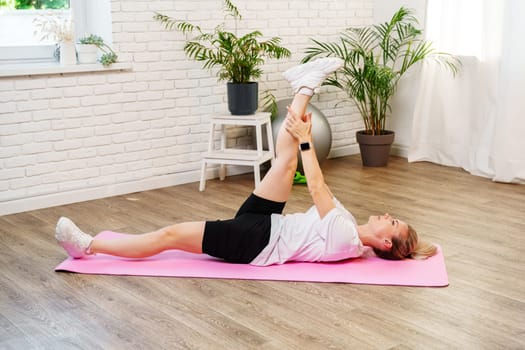 Woman doing floor exercises on a pink mat in a bright, plant-filled room